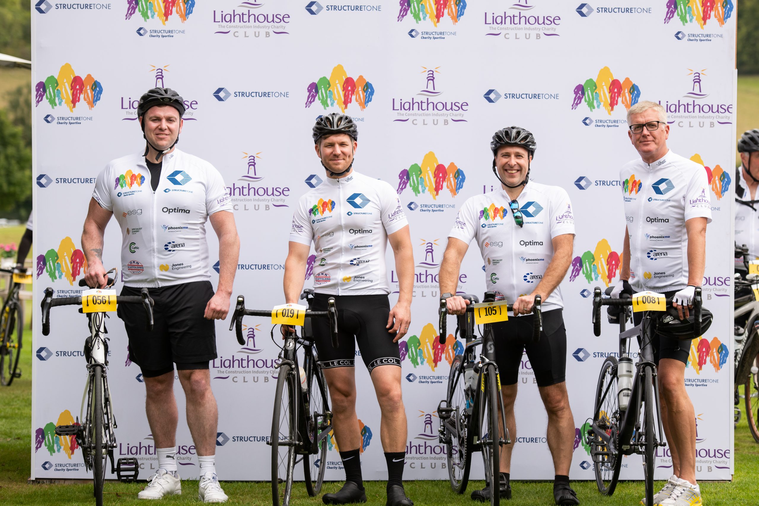 Four cyclists in matching gear smiling for a photo with their bikes.