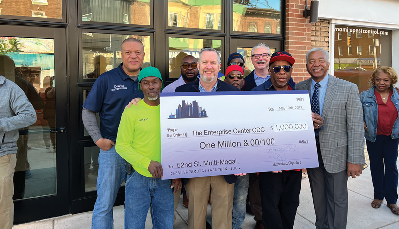 A group of people proudly holding a check in front of a building.