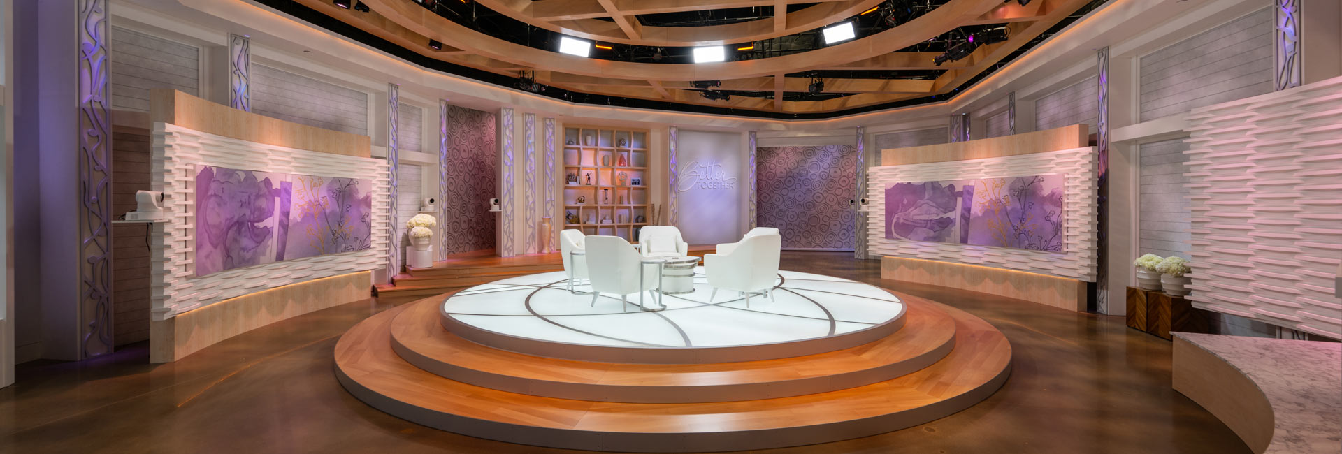 A talk show space with purple walls and white chairs.