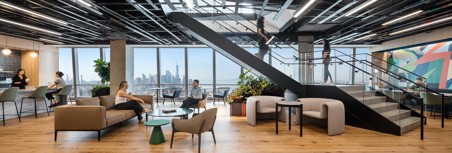 An open office area with couches and chairs underneath a featured staircase