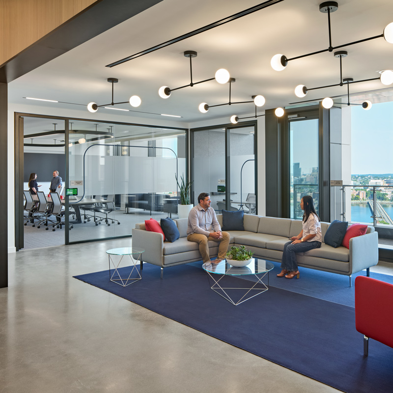 A contemporary office space featuring individuals seated on stylish couches, engaged in conversation and collaboration.
