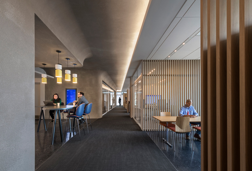 Hallway featuring floor to ceiling wood paneling and tables where people are working.