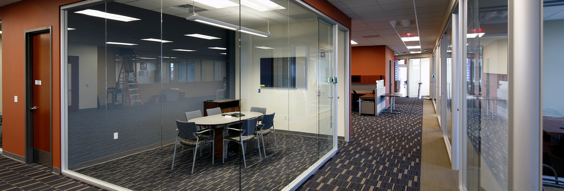 A modern conference room featuring glass walls and a large central table, designed for collaborative meetings.