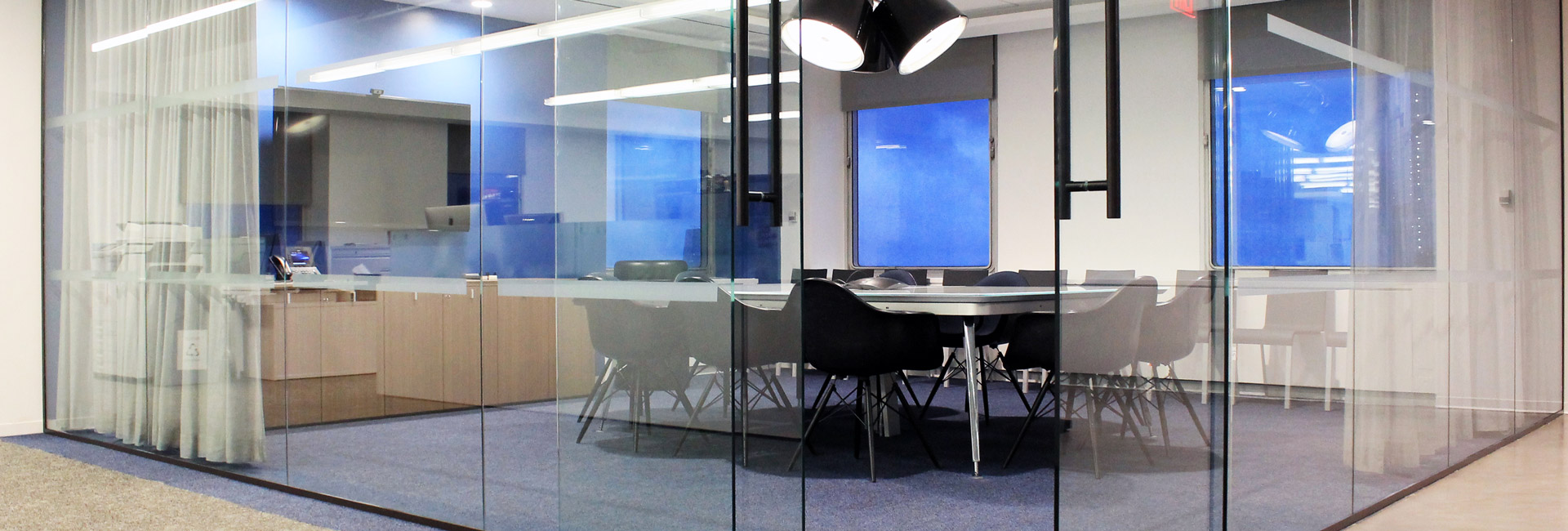 A modern office featuring a glass partition, equipped with a table and chairs for collaborative work.