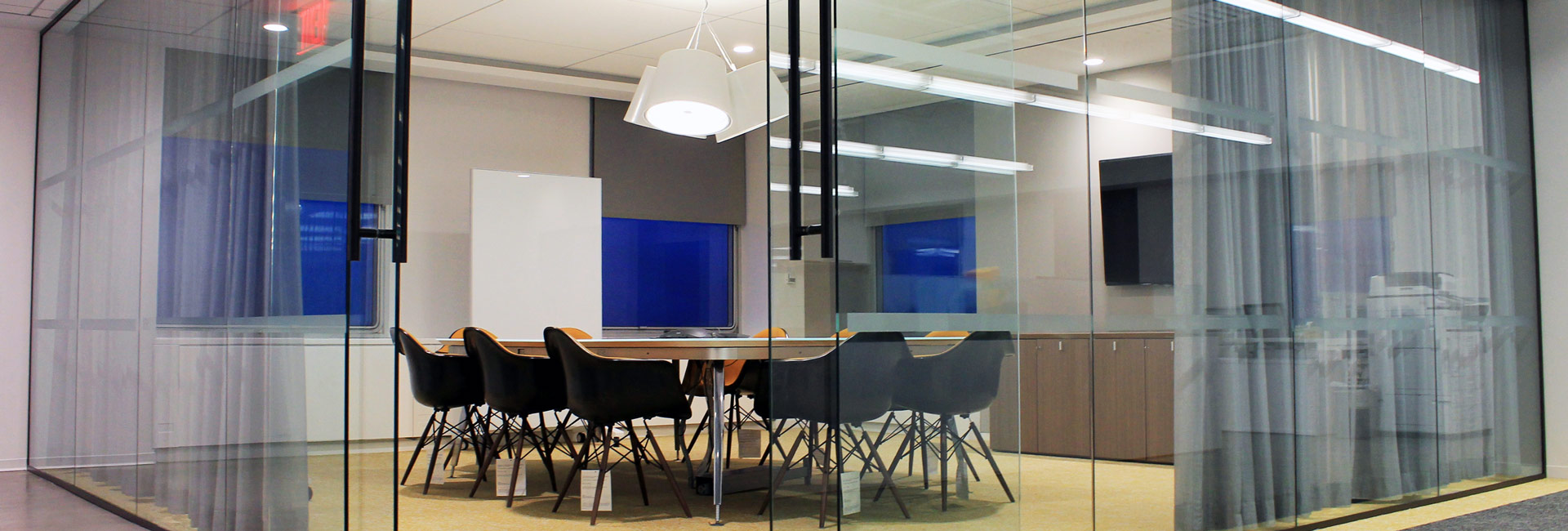 A modern office featuring a glass partition, equipped with a table and chairs for collaborative work.