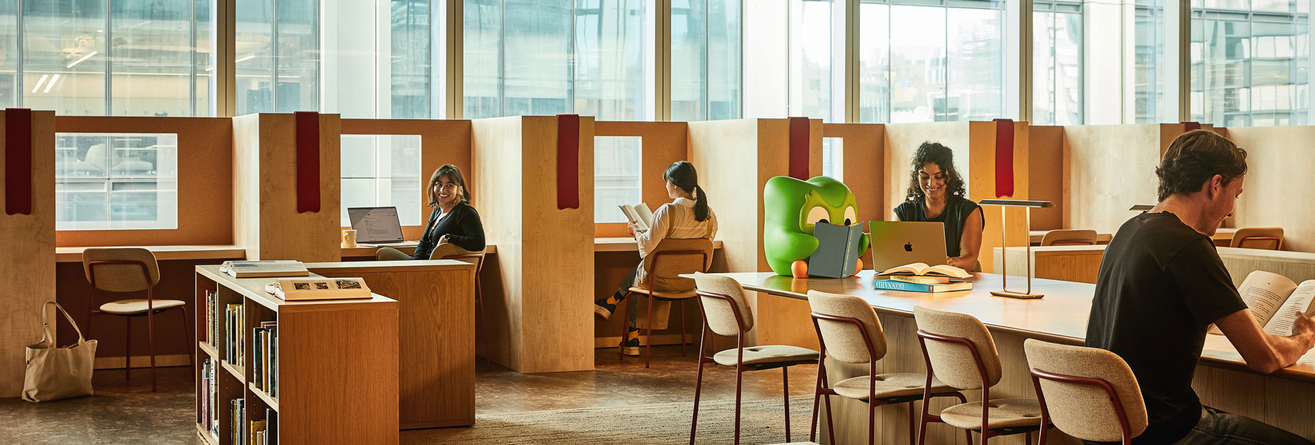 Employees at tables in a library, immersed in their work, with numerous books lining the shelves around them.