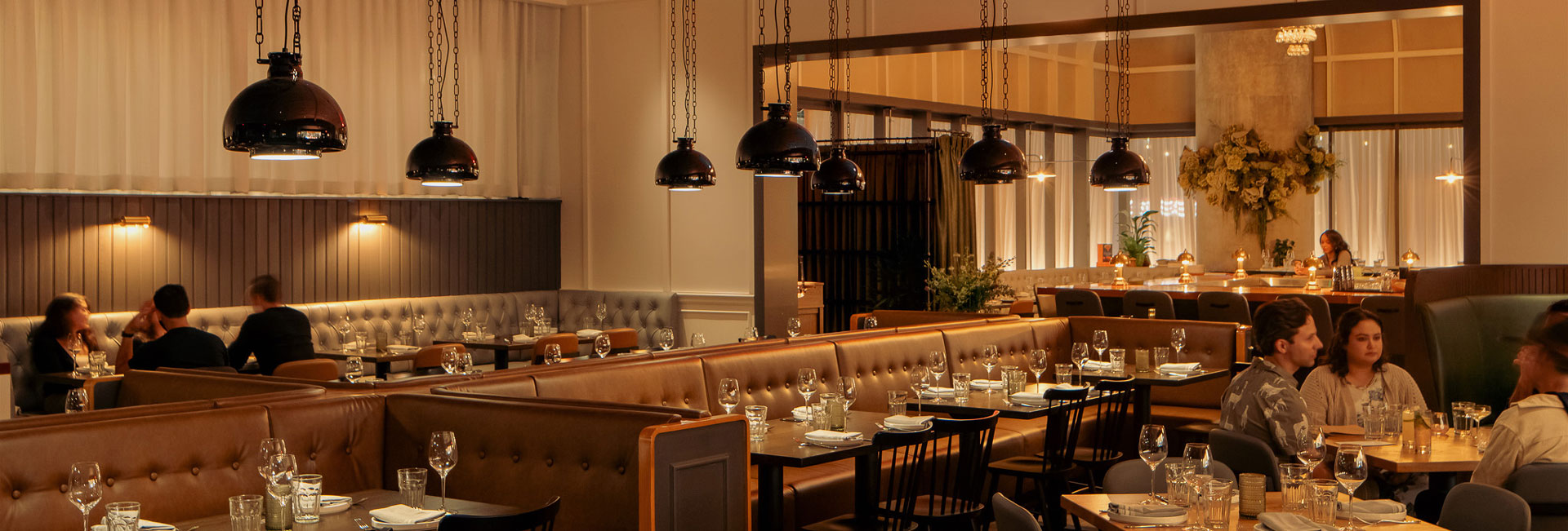 A bustling restaurant scene featuring patrons at tables beneath warm, hanging lights, creating a lively atmosphere.