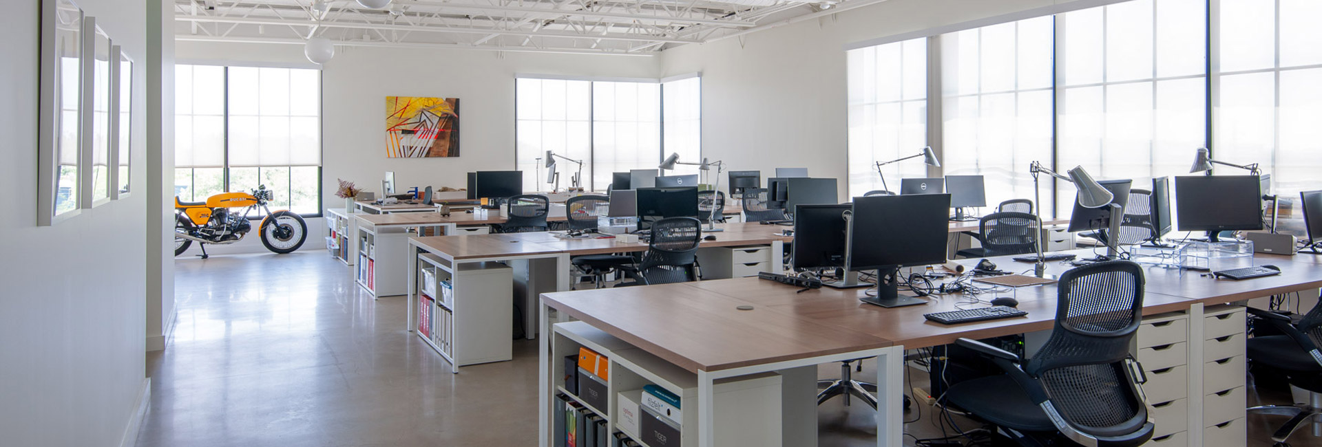 A spacious office featuring numerous desks equipped with computers, showcasing a collaborative work environment.