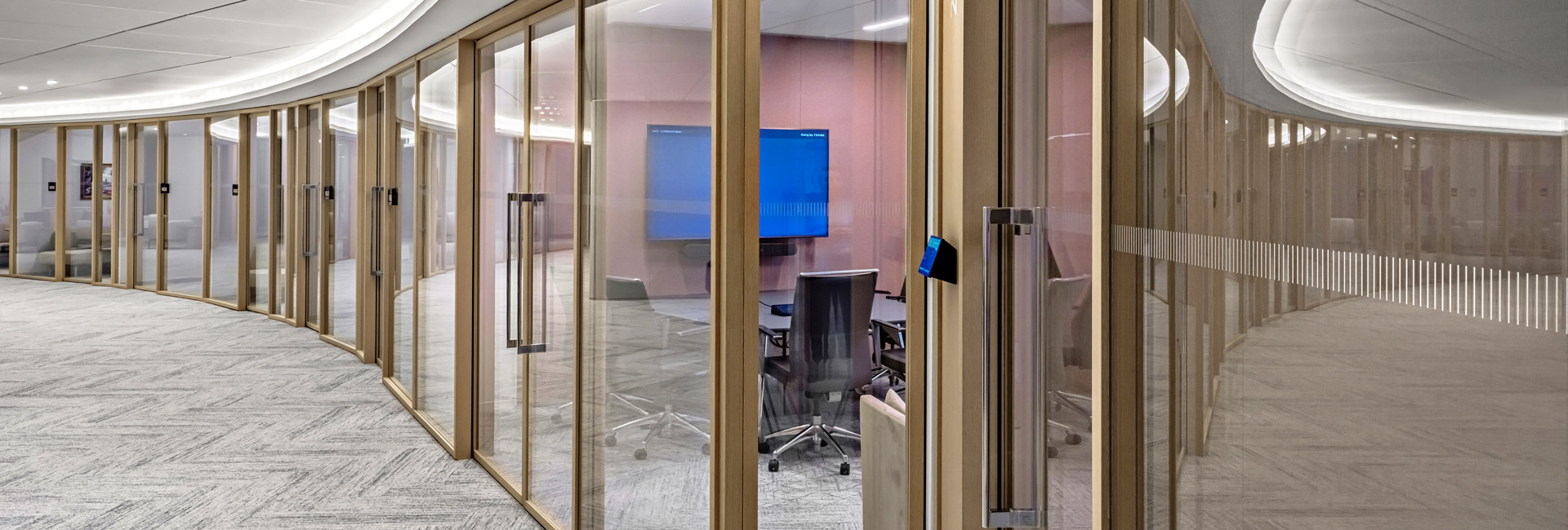 A lengthy corridor with glass walls and meeting rooms.