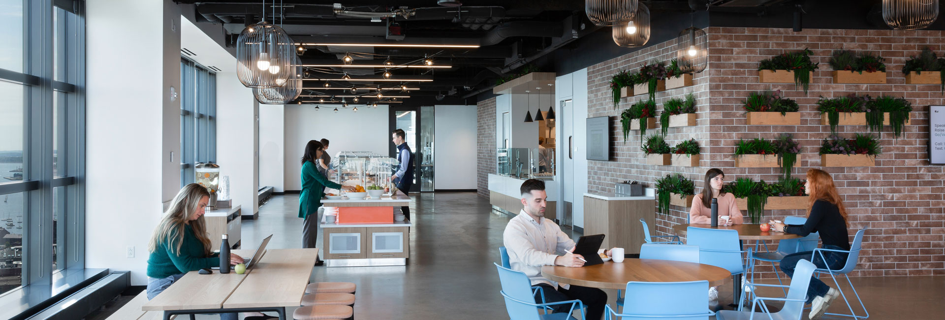 Individuals seated at tables in a well-lit office, featuring expansive windows that enhance the workspace.