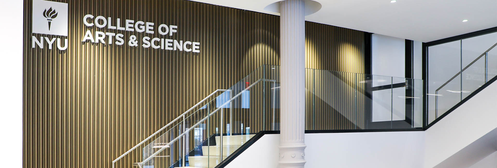 NYU College of Arts and Sciences lobby with white stairs and wood accent wall and NYU logo as well as metal security turnstiles renovation by Structure Tone New York.