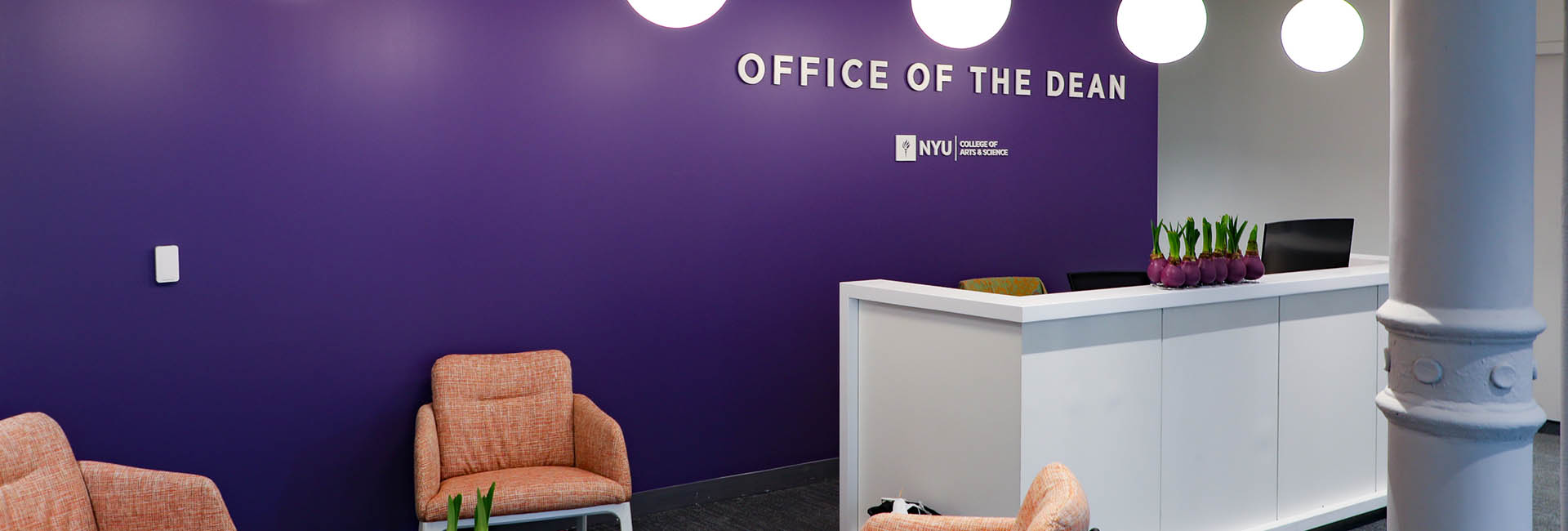 Reception area of the Office of The Dean with purple accent wall with logo and peach seating for NYU College of Arts and Sciences renovation by Structure Tone New York.