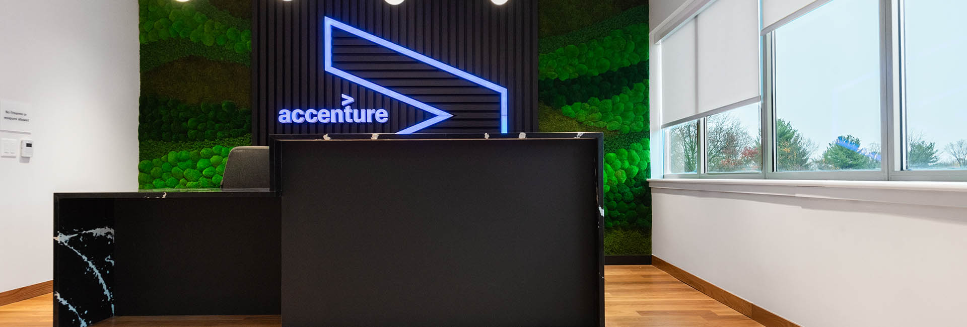 Office reception area showcasing a sleek desk against a bright green wall, enhancing the space's modern design with a glowing Accenture logo sign.