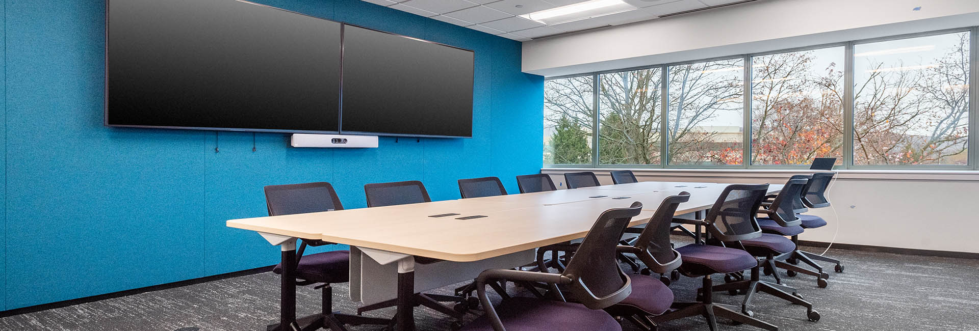 A conference room featuring a large screen at the front with a vibrant blue accent wall and several chairs arranged for attendees at Accenture.