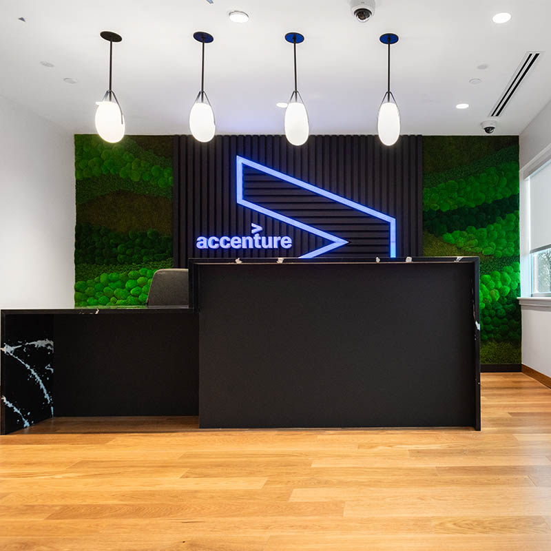 Reception area with glowing Accenture word sign on black and green background wall and a black reception desk.