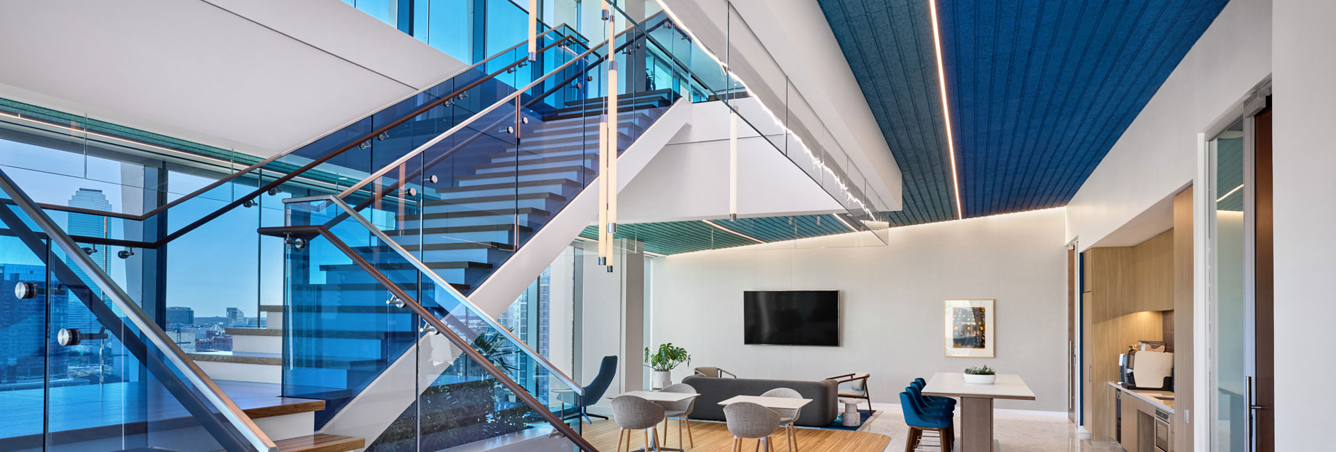 A modern office area featuring blue walls and sleek glass stairs, creating a stylish and open atmosphere.