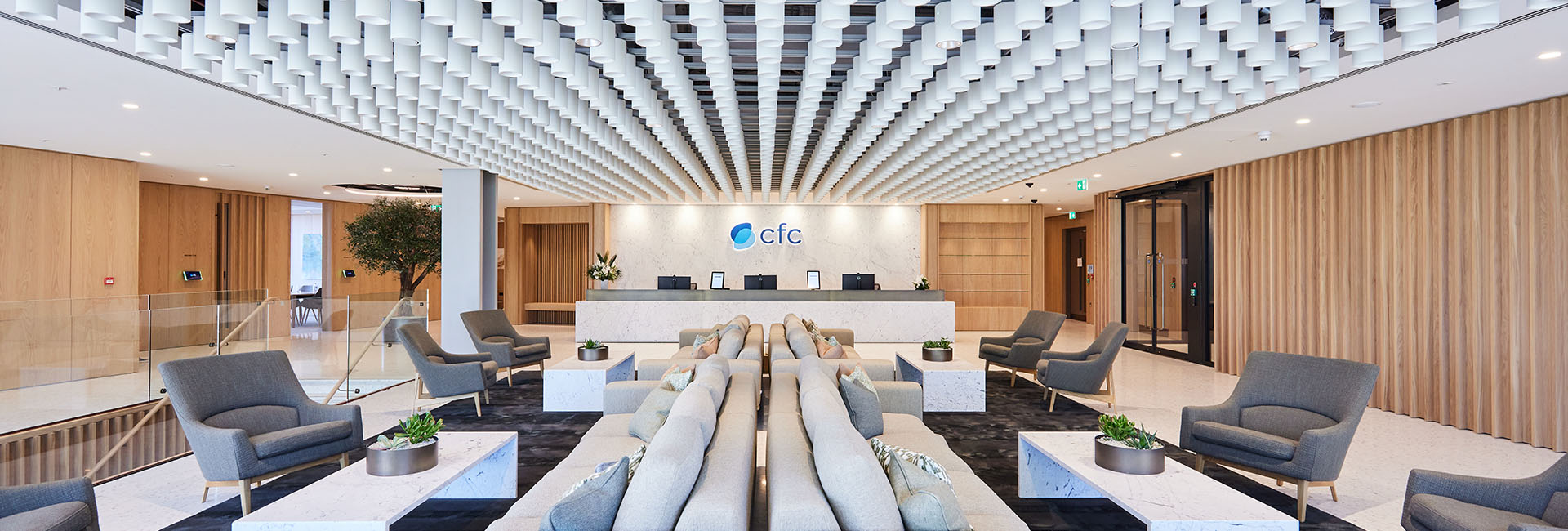 CFC Underwriting lobby with couches and grey chairs and wood wall accents with the reception deck in center with blue logo above