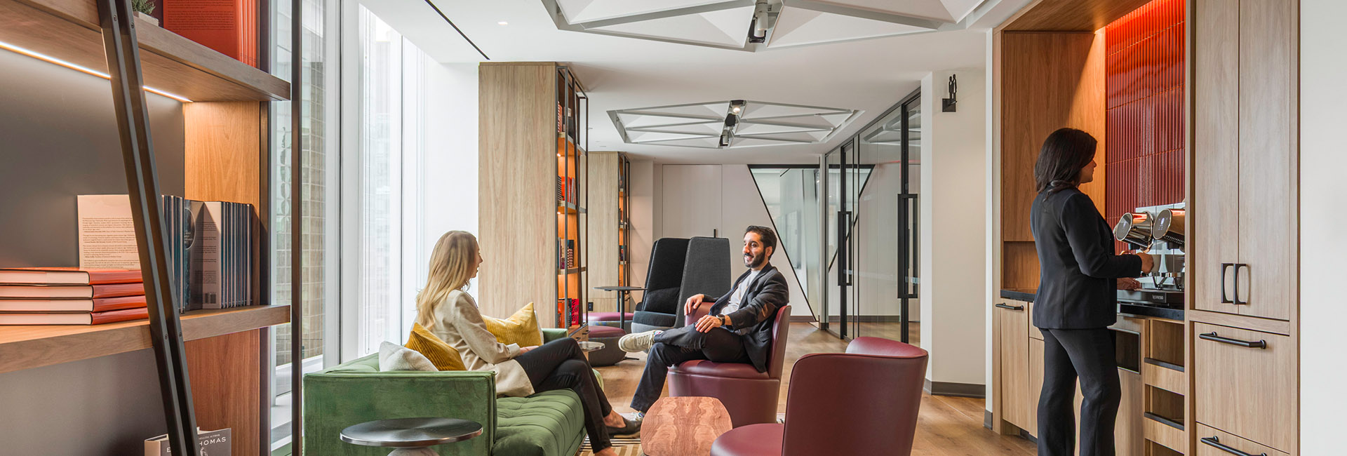 two people sitting in a break area with green and brown chairs and a kitchenette