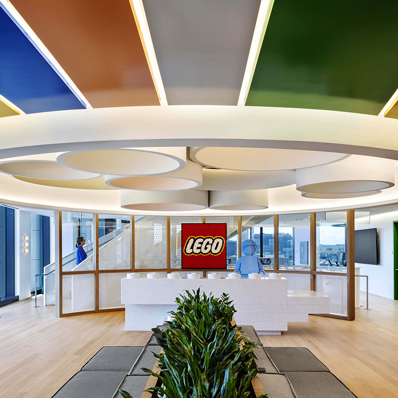 LEGO Boston HQ built by Structure Tone Boston image of colorful ceiling accent, Lego block reception desk, plants and seating benches.