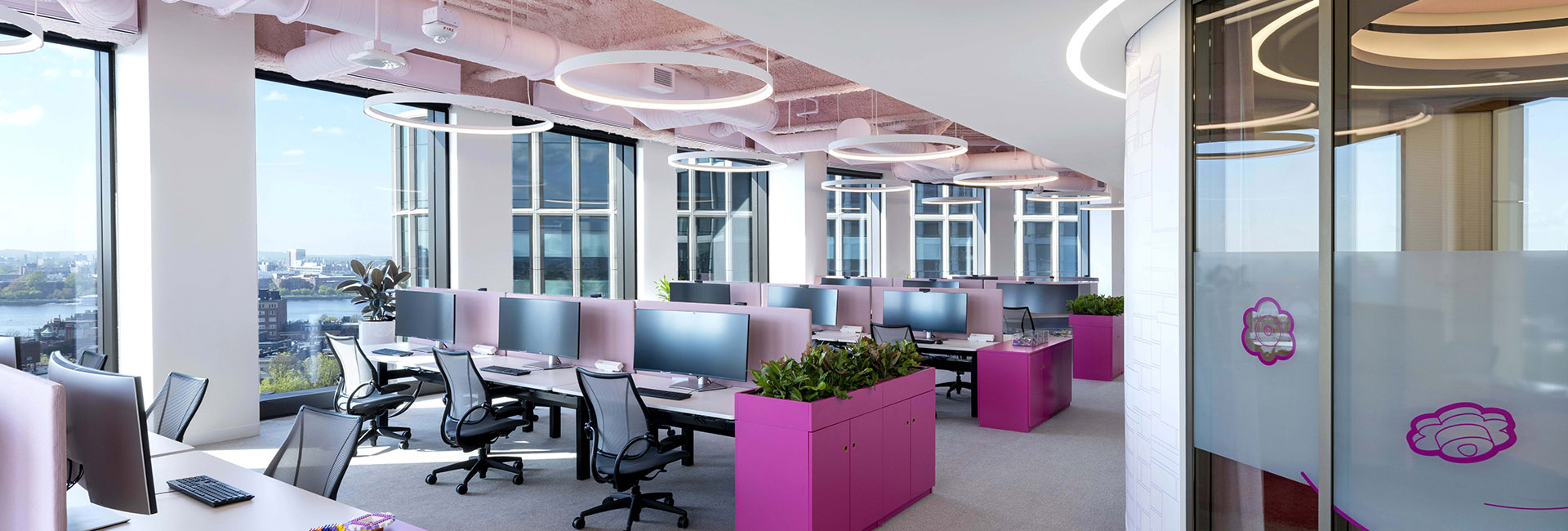 Lego HQ Boston desk and work area with bright fuchsia accents circular lighting on ceiling and glass doors with wall of windows built by Structure Tone Boston