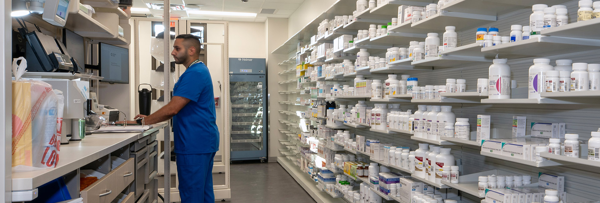 University Health Wheatley image of pharmacy worker in a pharmacy lab with rows of shelfs an medicine