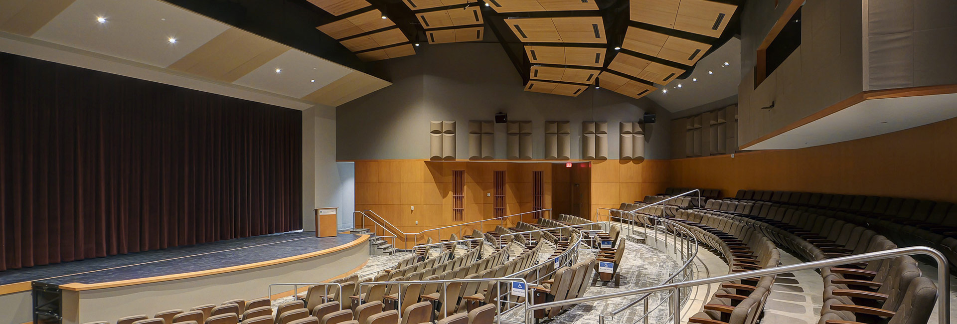 Modern auditorium with tiered seating, curved aisles, and a stage with closed curtains.
