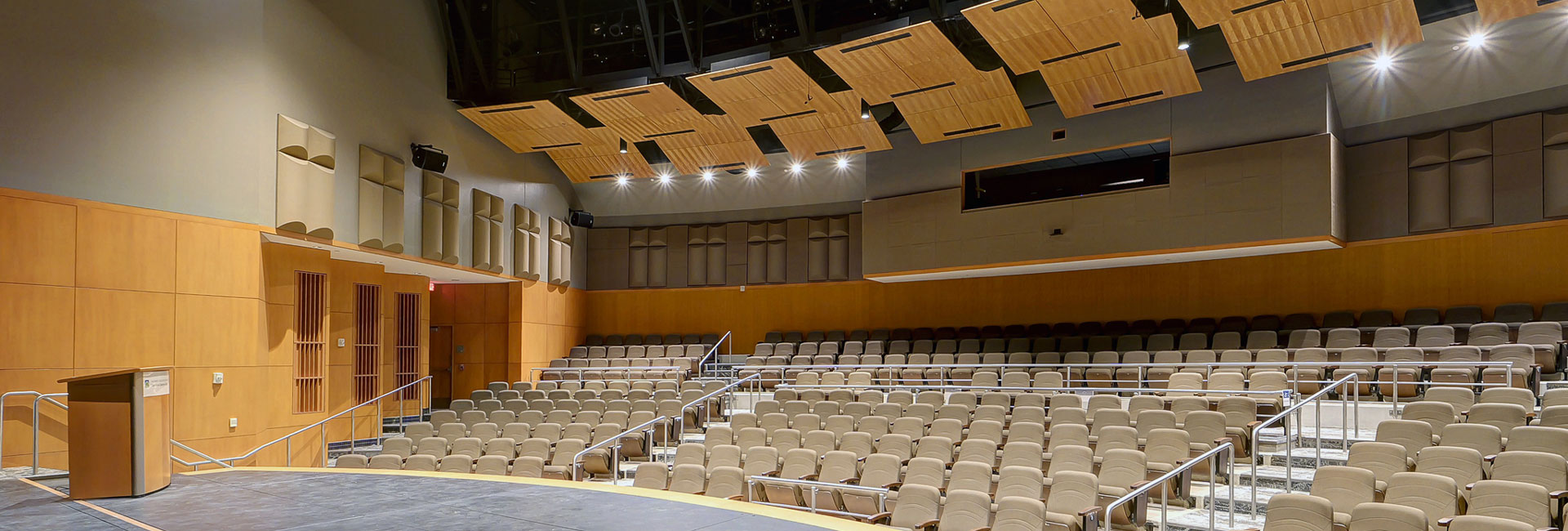 View from the stage of an auditorium with tiered seating and suspended wooden acoustic panels.
