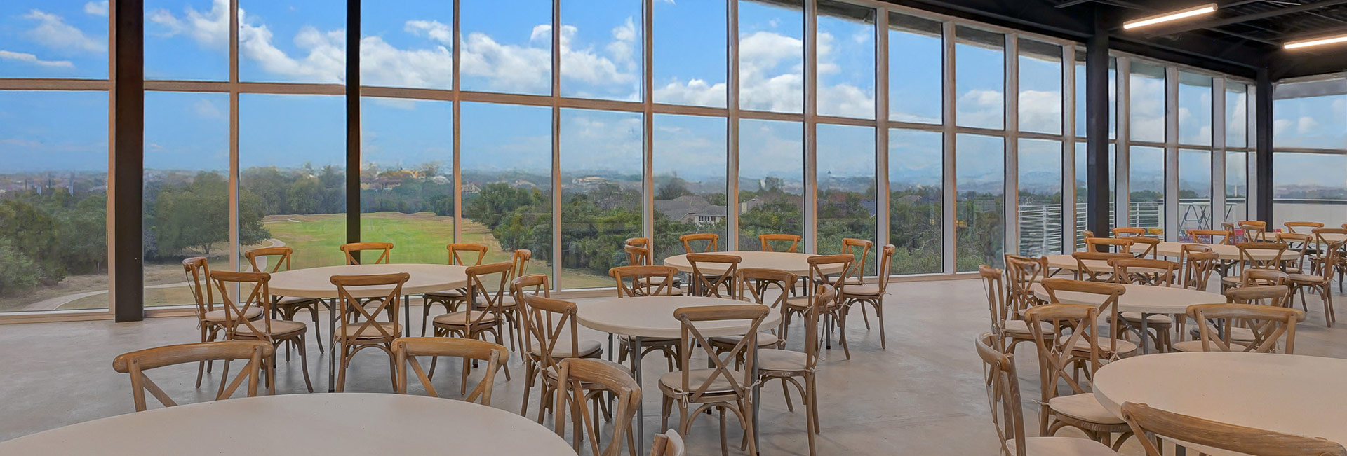 Banquet area with several tables and chairs with flooring to ceiling windows overlooking a golf course.