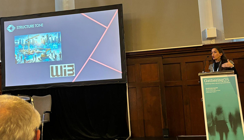 UK CitA person at podium speaking to audience with a video on stage