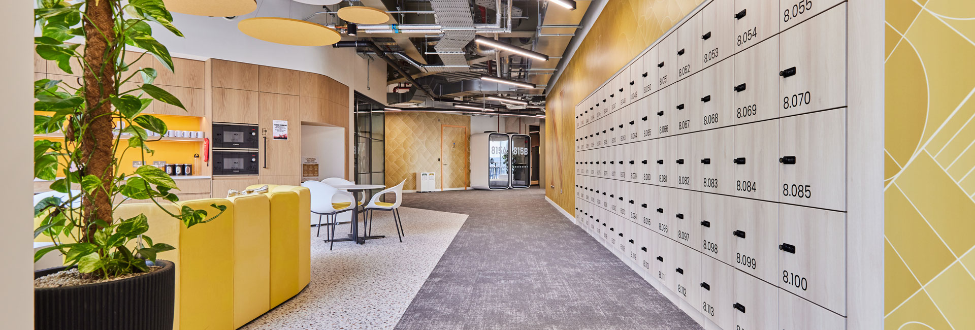 A hallway with a wall of locker spaces and an open kitchen area of students to use.