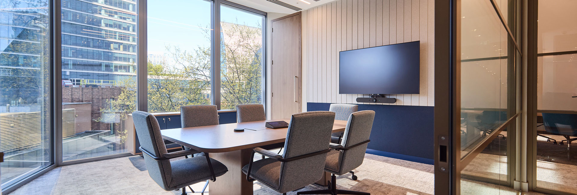 A conference room with a table and chairs and monitor display on the wall