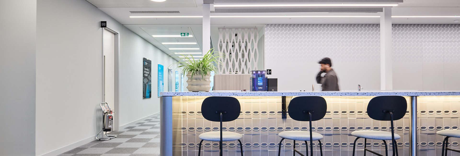 Kitchen area that holds a coffee machine and has barstool chairs for employees to be able to sit