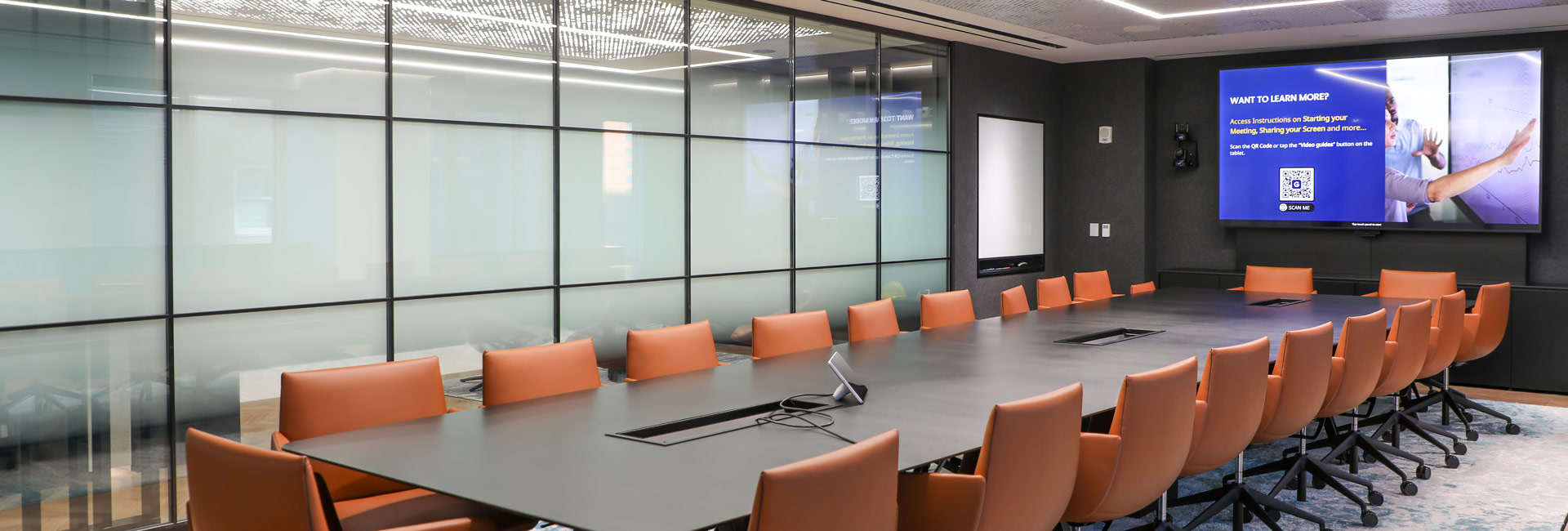 A large conference room with a long table with several chairs around it.