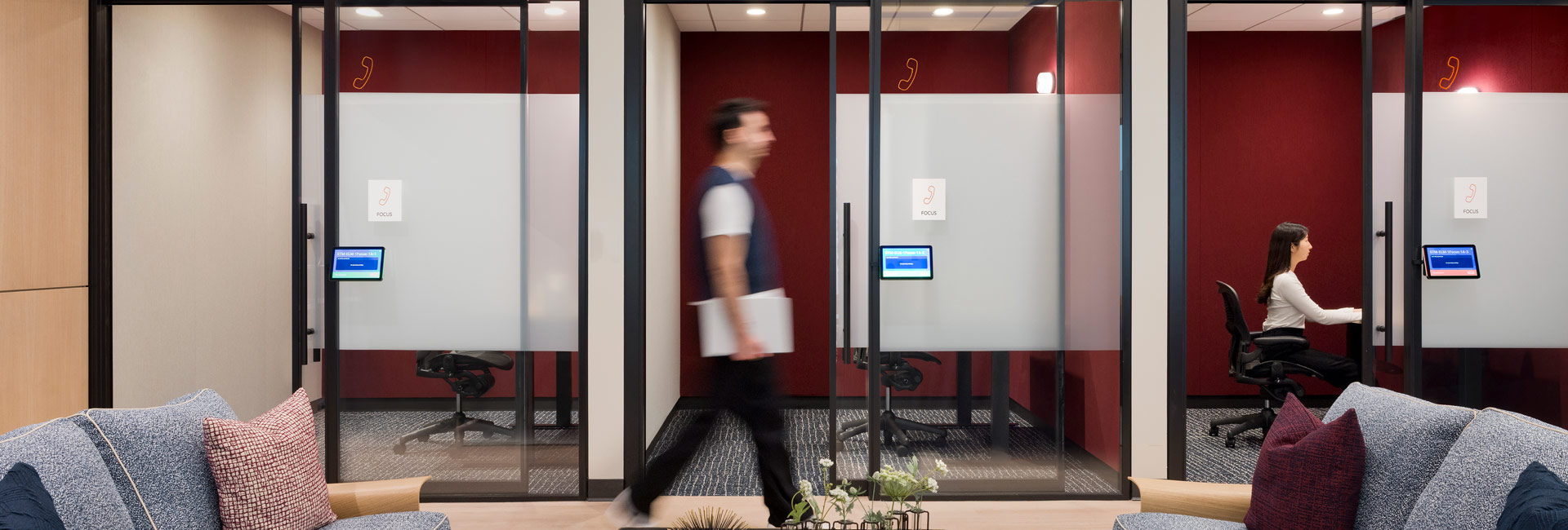 An employee walking past several smaller conference rooms with glass walls.