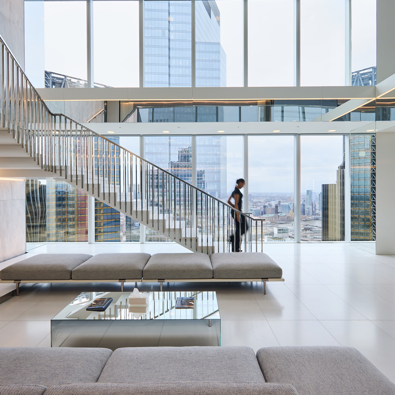 A woman walking down a flight of stairs in an open office space overlooking the London skyline.