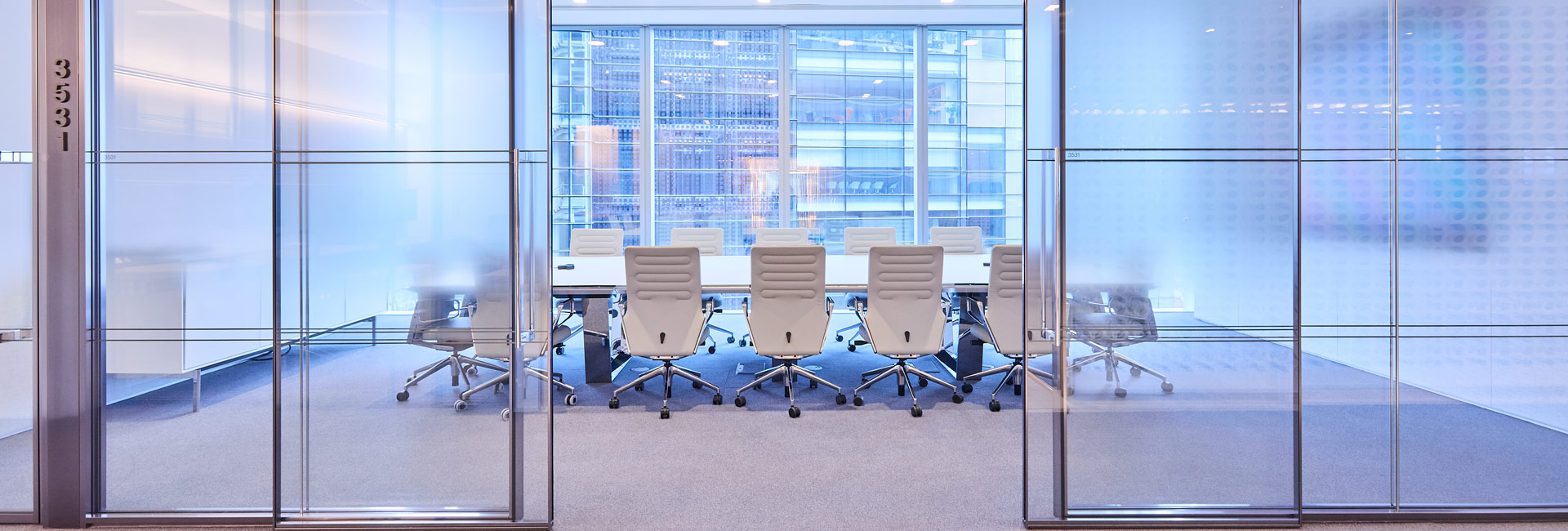A large conference room with a long table and several large white chairs around it.