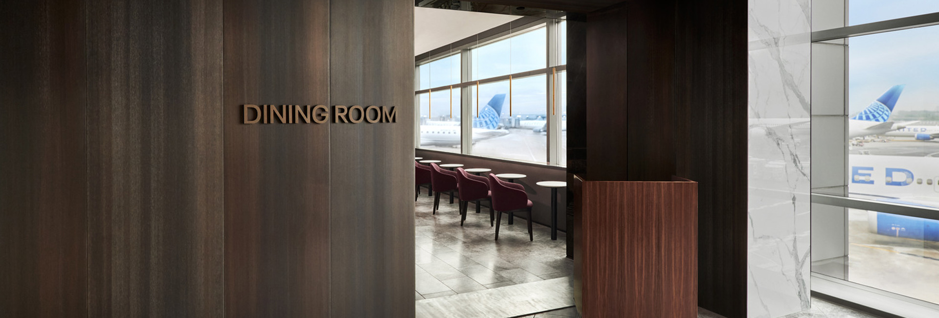 Wood-paneled entrance to the Polaris Lounge dining room with runway views and United aircraft visible through large windows.