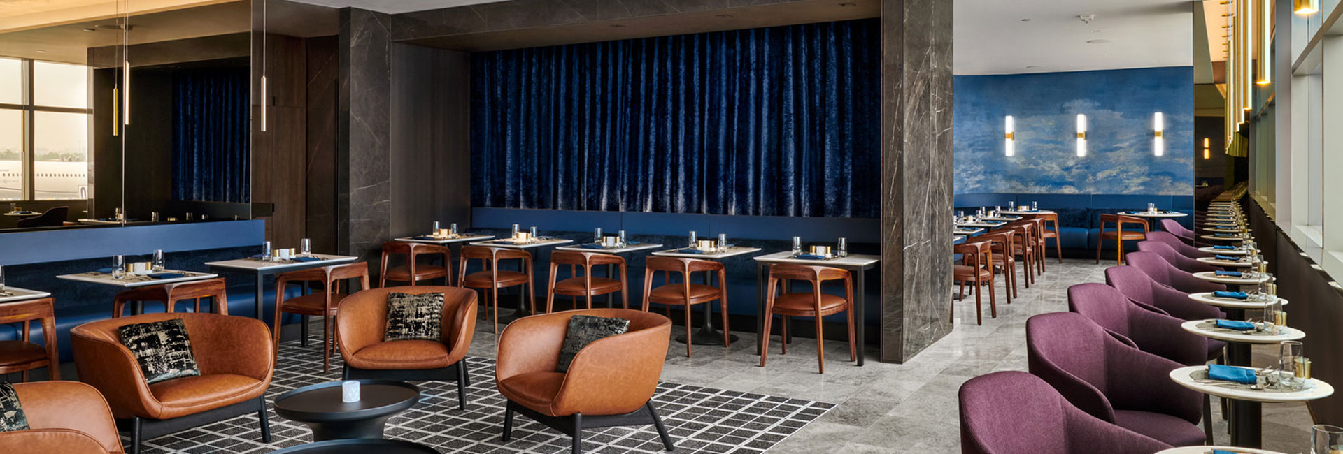 Expanded Polaris Lounge dining room with blue banquettes, leather lounge chairs, purple seating, and floor-to-ceiling windows.