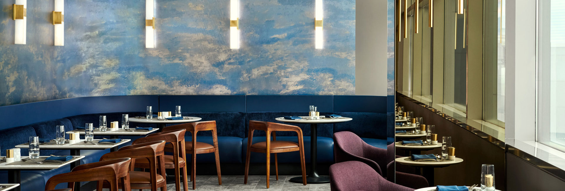 United Polaris Lounge dining area with blue banquette seating, wood chairs, textured walls, and mirrored window panels.