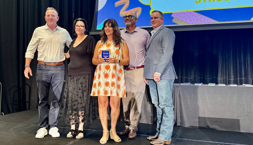 Five colleagues pose onstage as a woman holds an award during a ceremony.