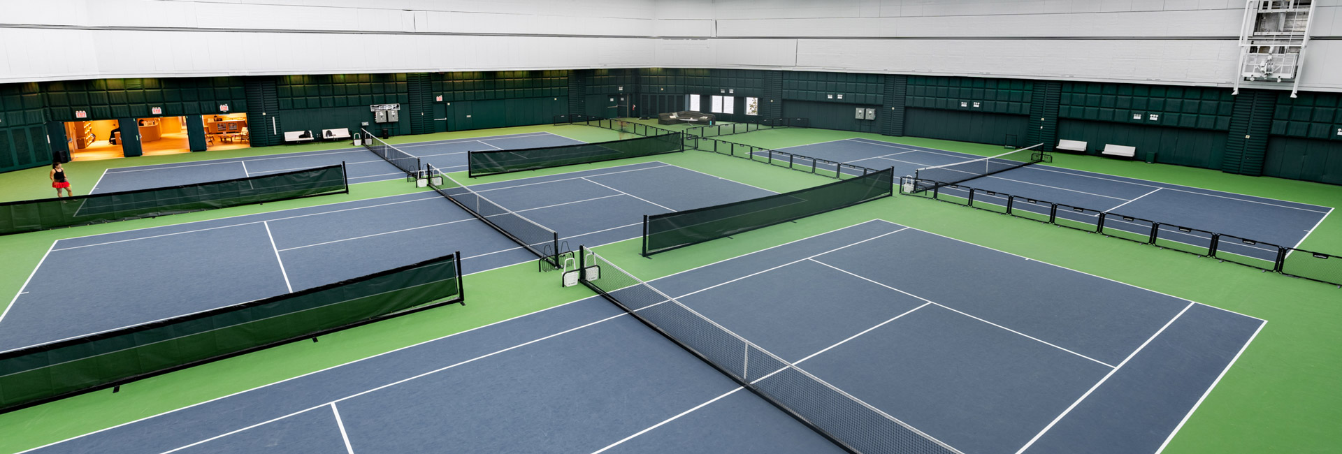 Multiple blue-and-green indoor tennis courts inside the double-height Hudson River Tennis Club.