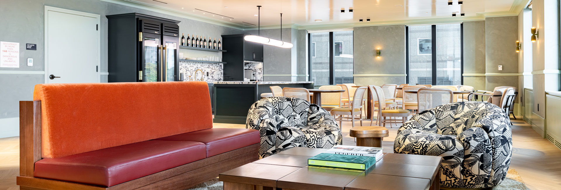 Club lounge with colorful seating, café tables, and a bar overlooking large windows.