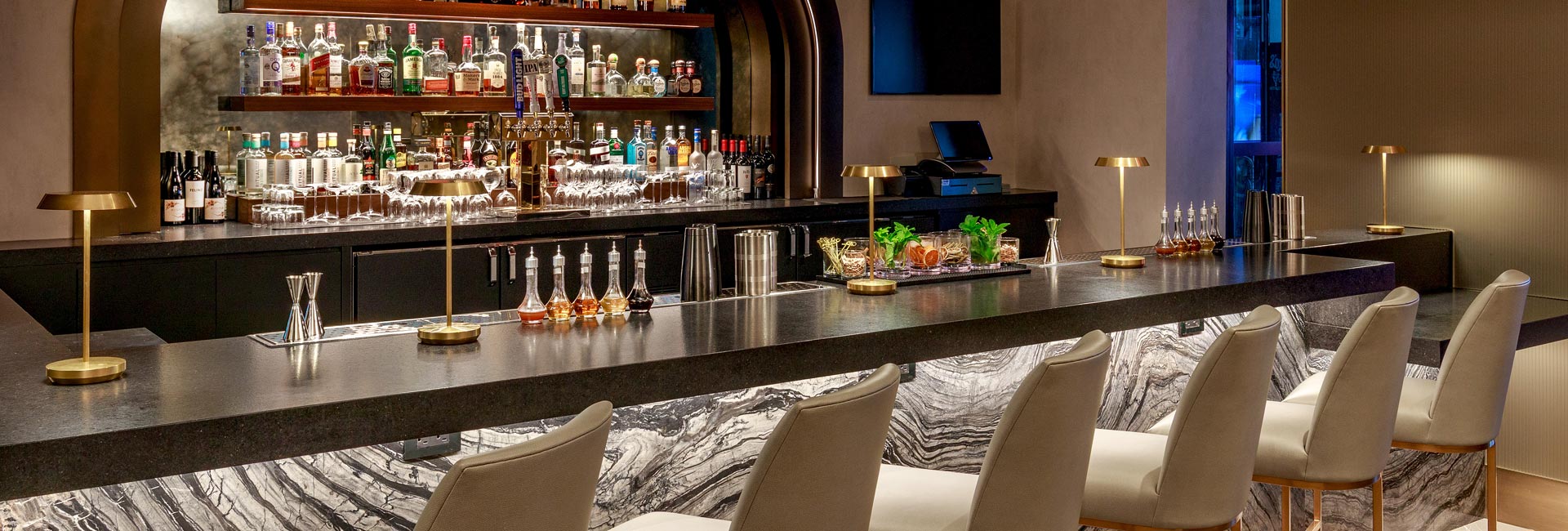 Bowtie Bar at the Renaissance New York Times Square Hotel features marble finishes, upholstered seating, and brass lighting.