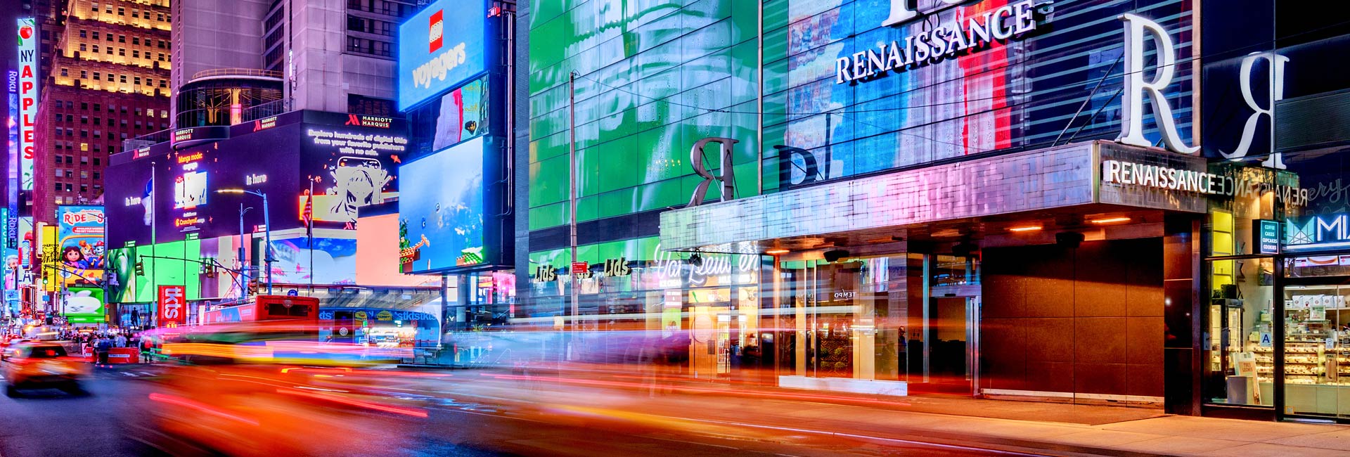Renaissance New York Times Square Hotel entrance surrounded by colorful billboards and passing traffic at night.