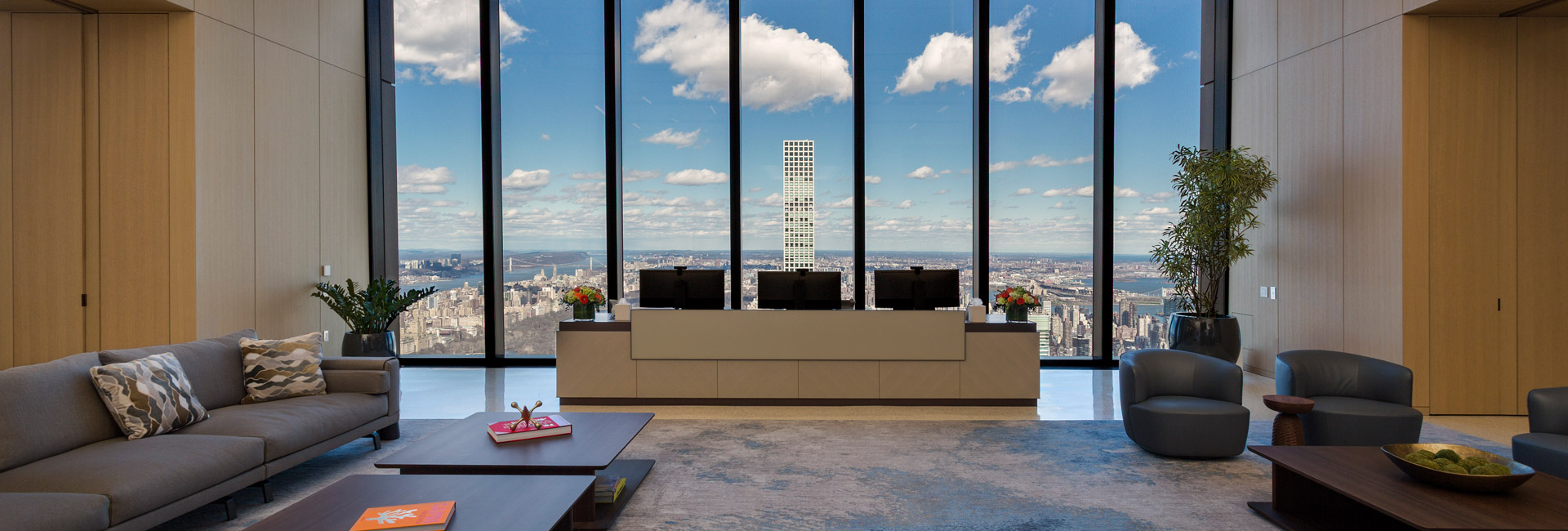 Spacious reception lounge with contemporary seating, a central welcome desk, indoor plants, and panoramic views of New York City.