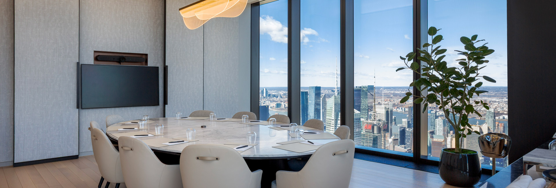 Executive meeting room with a marble table, white chairs, integrated video display, and floor-to-ceiling windows overlooking New York City.