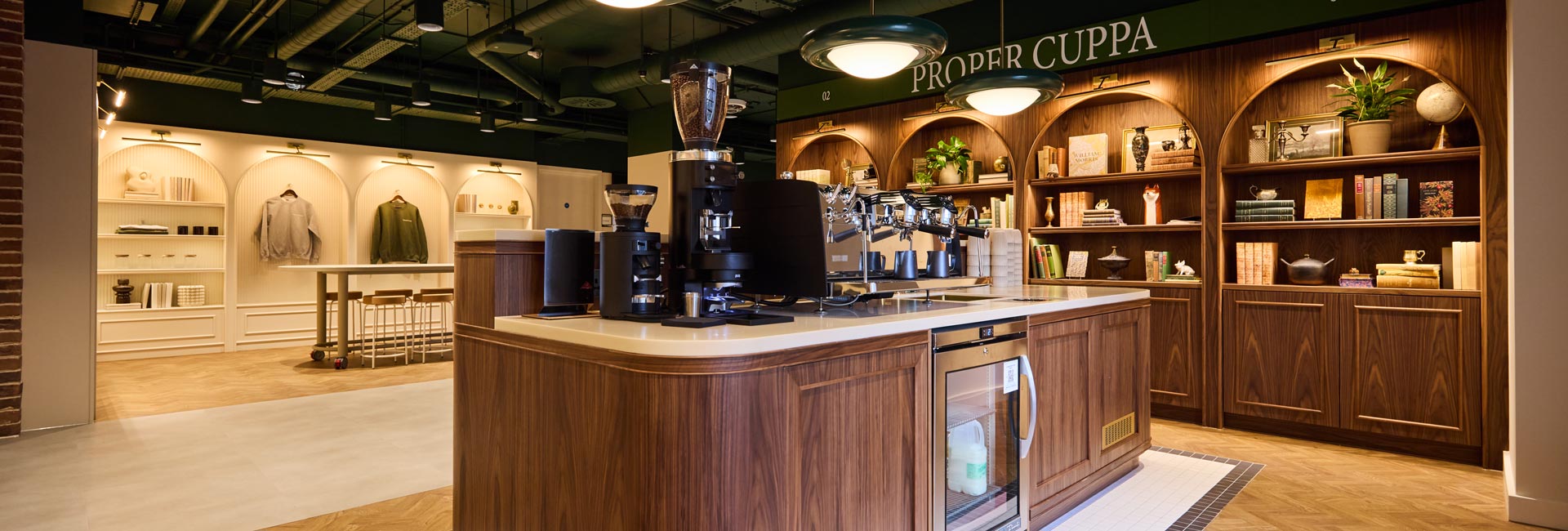 Pinterest office coffee bar with a curved wooden counter, espresso machine and arched shelving filled with books, plants and decorative objects.
