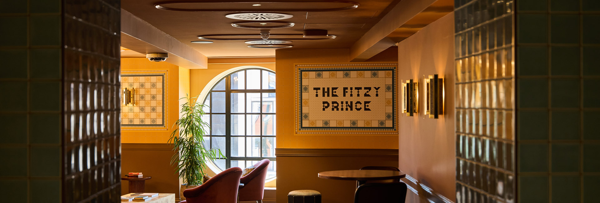 Warmly lit office lounge inspired by a traditional pub, featuring tiled walls, a circular window and “The Fitzy Prince” signage.