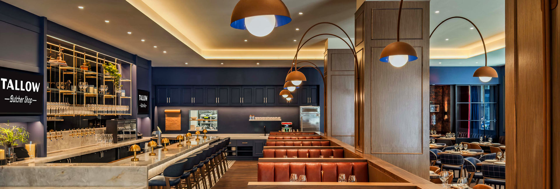 Tallow Butcher Shop dining area with a marble bar, leather booths, curved pendant lights, and dark blue finishes.