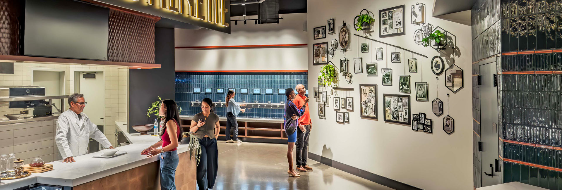 Visitors explore a food counter and gallery wall featuring framed photographs and plants inside Shaver Hall.